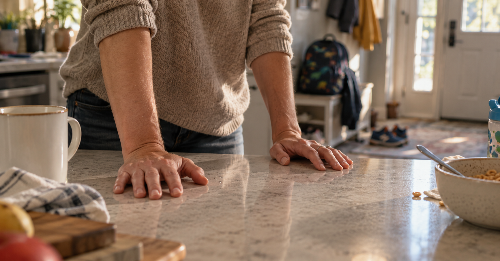 Hands braced on a kitchen counter during a busy family morning, showing the daily strain of lower back pain when waking up