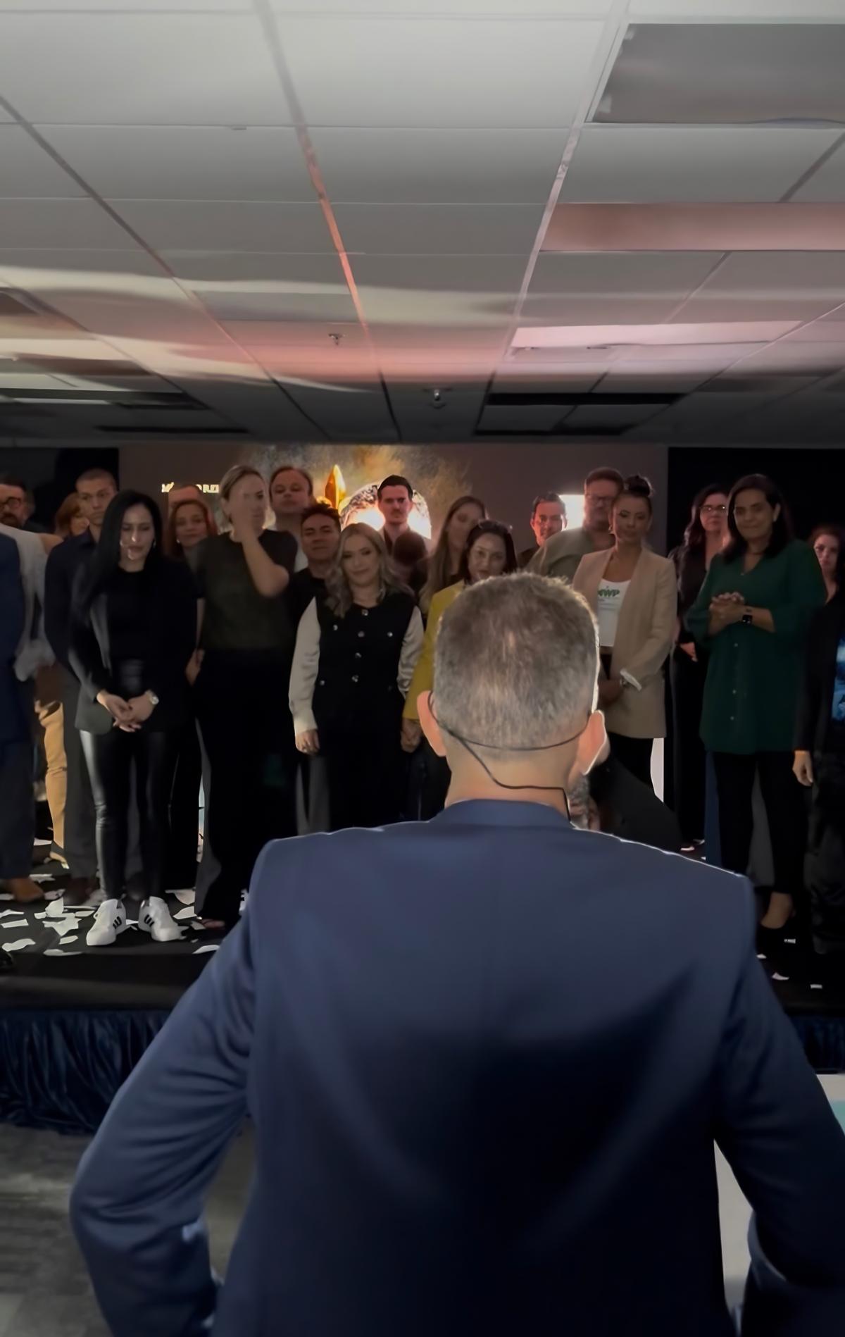 Mentor diante de participantes em pé durante um encontro do PLANO CAPITAL