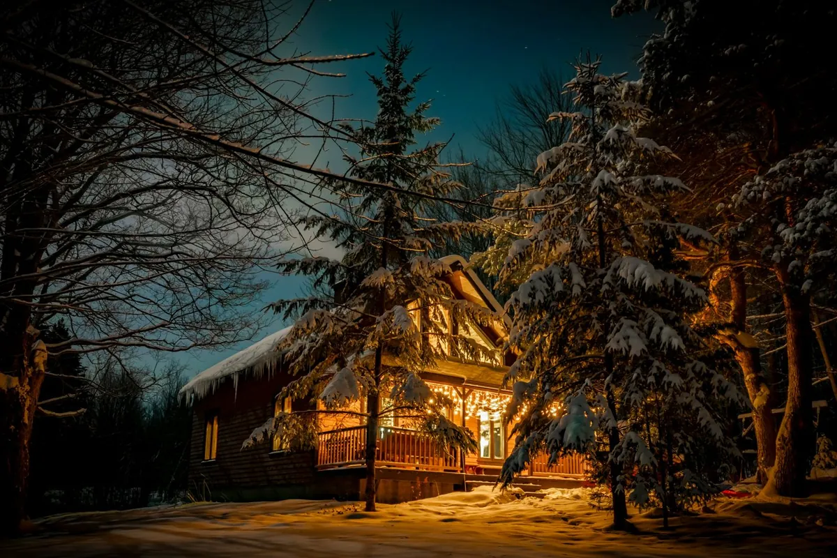 A wooden chalet glowing with warm light among snow-covered pines at night