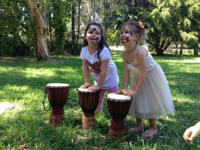 Two young girls playing djembe drums on the grass at an African Beat kids' birthday party in Sydney