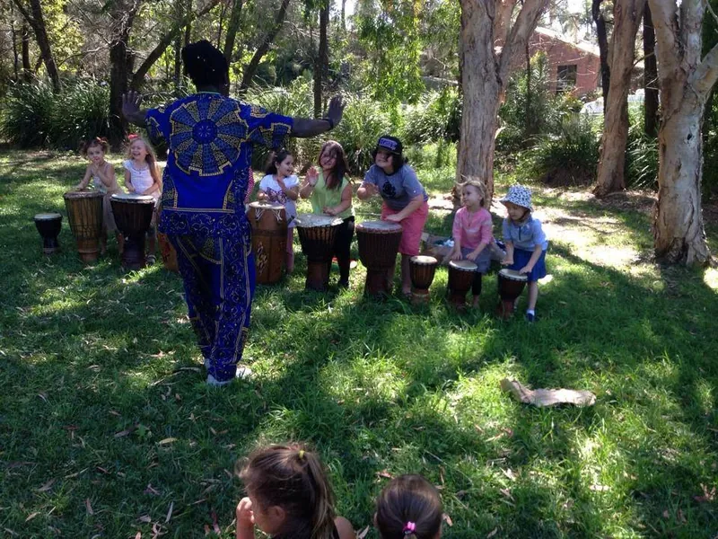 African Beat performer dancing in a park at a Jungle Beats children's party while children watch