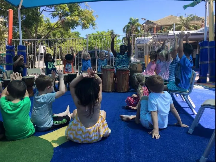 Young children drumming with African Beat performers outdoors at a child care centre