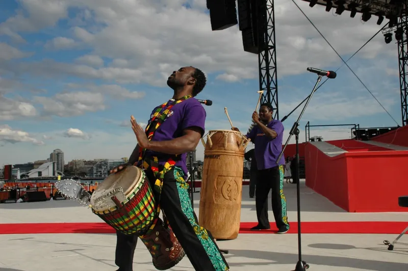 African Beat drummer performing on an outdoor stage by the water