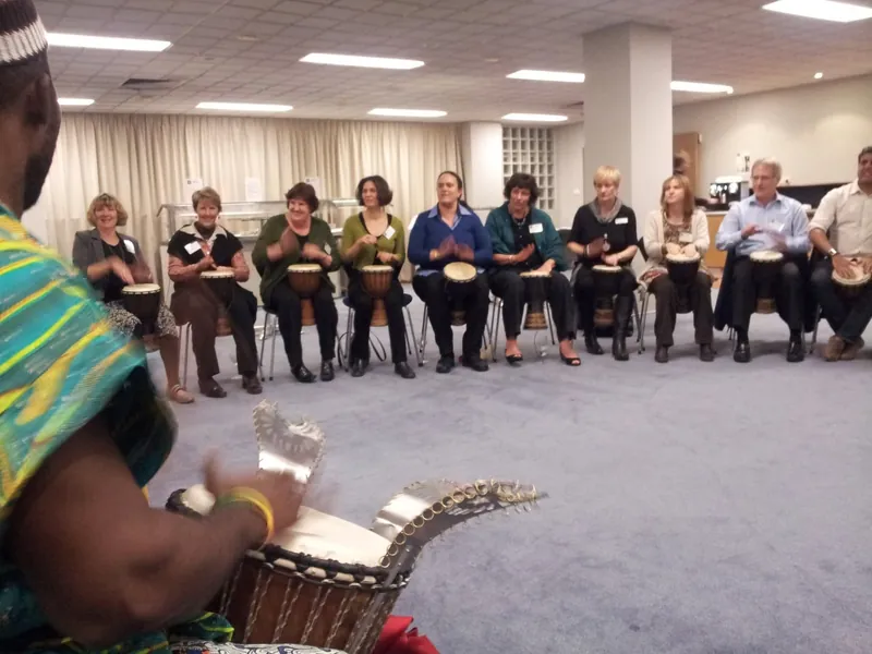 Staff seated in a circle playing drums during an African Beat team-building experience