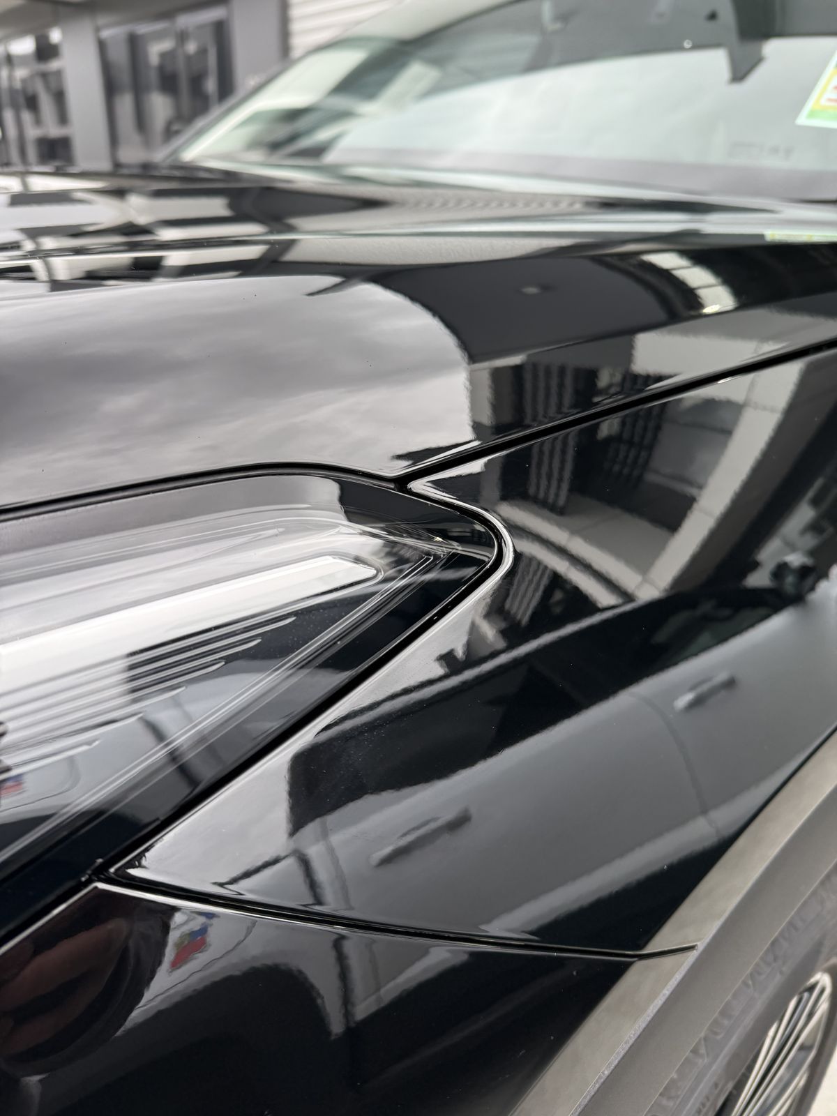 Close-up of gloss paint protection film on a black car's headlight and front guard, with mirror-like reflections