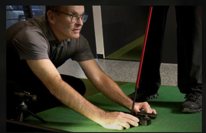 A coach positions a Putt Lab sensor beside a golfer's putter in the Putting Studio.
