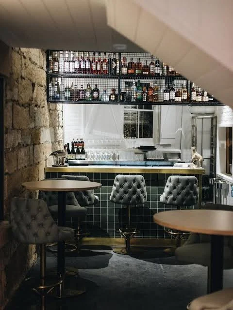 Green-tiled bar and upholstered chairs framed by a historic stone arch