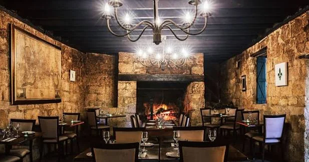 Historic stone dining room with chandeliers and a glowing open fireplace