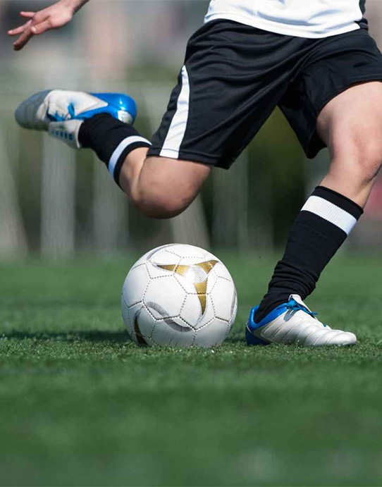 Jovem futebolista a conduzir a bola durante um jogo em relvado sintético