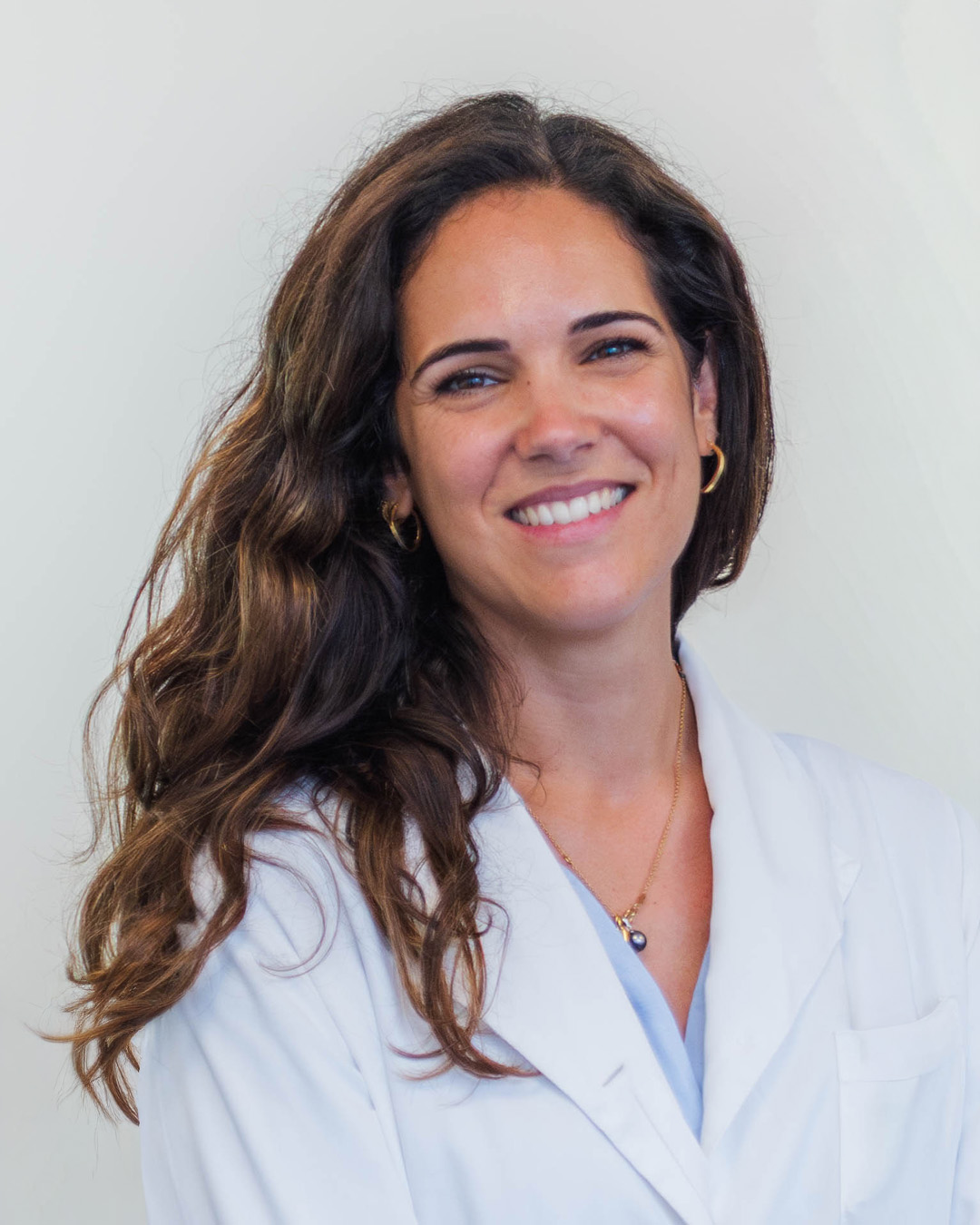Dra. Filipa Gonçalves Pereira sorridente, à secretária do consultório, com um modelo anatómico do joelho