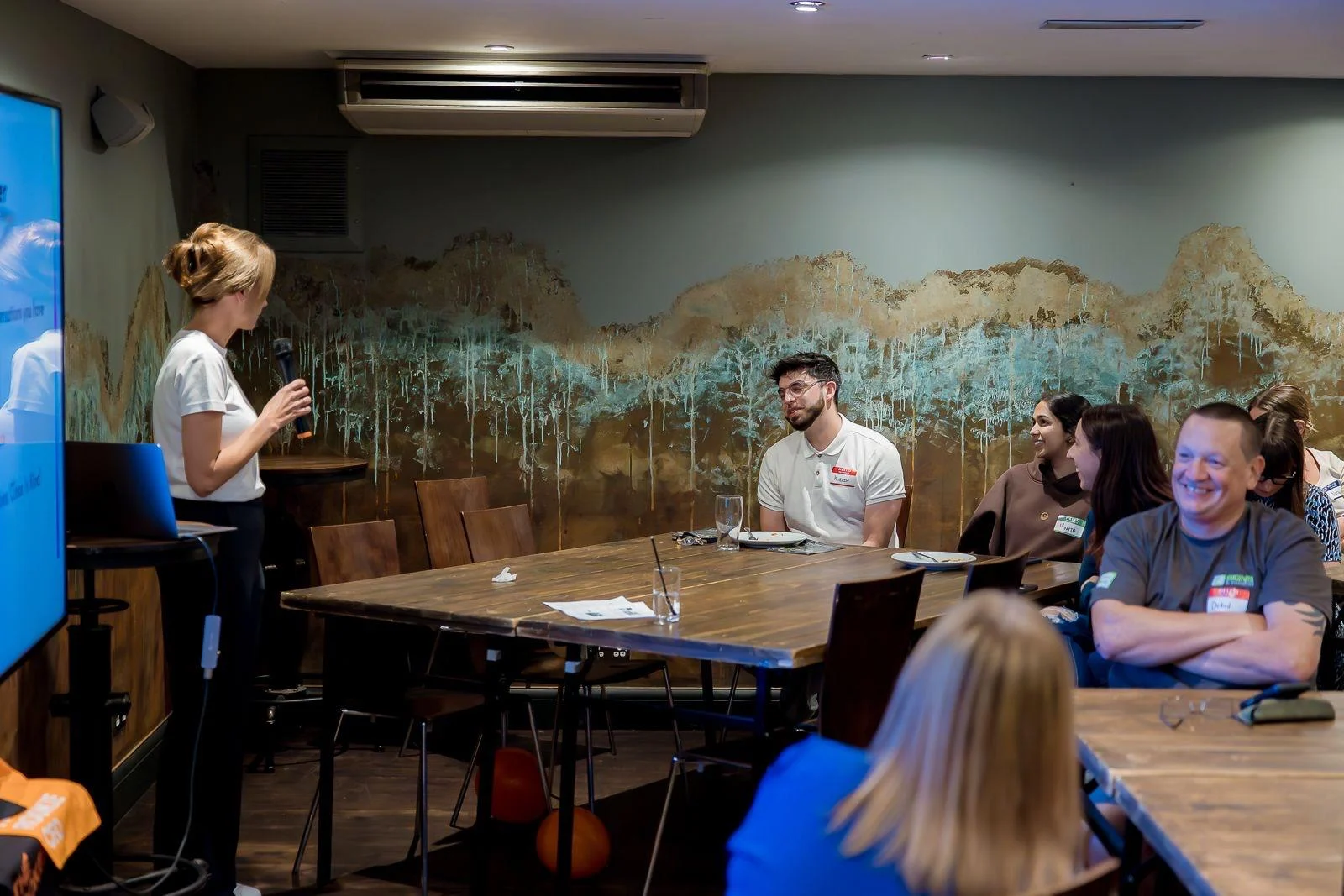Beth Turner speaking with a microphone to a smiling group of workshop attendees