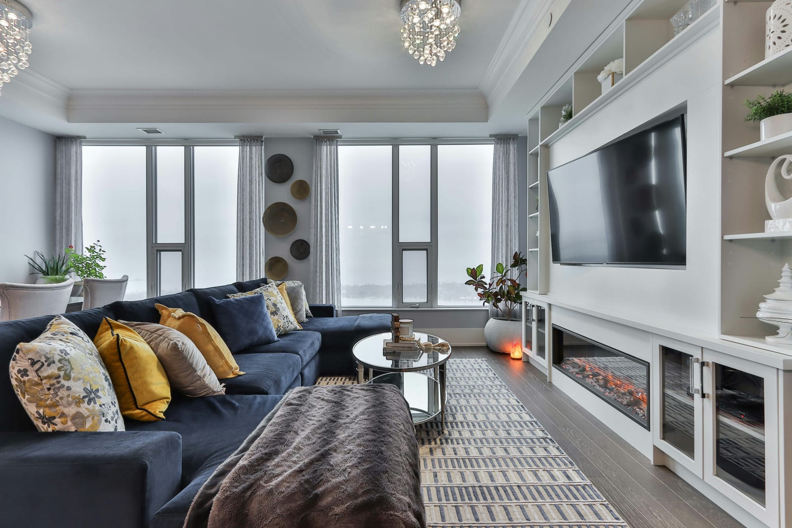 A condo living room with a grey sofa, warm cushions and the skyline through the window