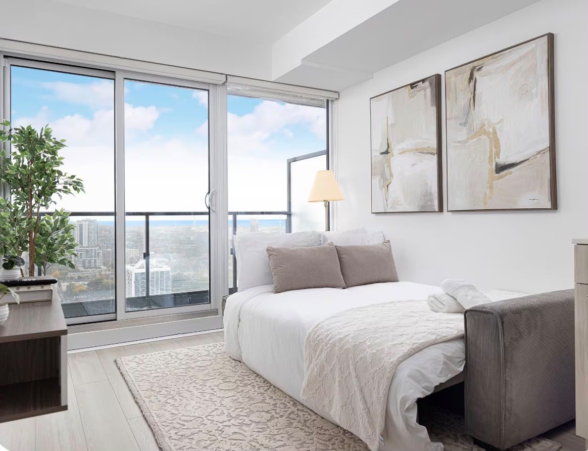 The second bedroom with a pull-out sofa bed and floor-to-ceiling windows over the city