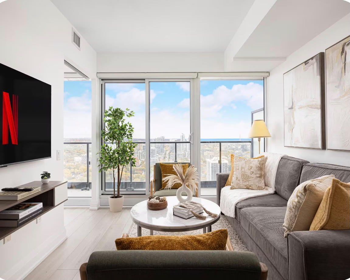The living room with a wall-mounted TV, balcony doors and a view over downtown Toronto