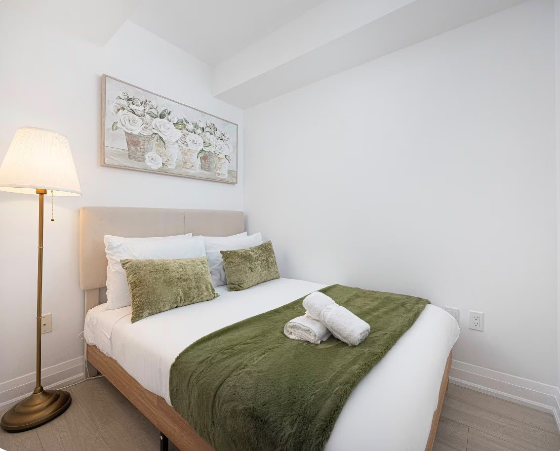 A cosy bedroom with a green throw, fresh towels and a brass floor lamp