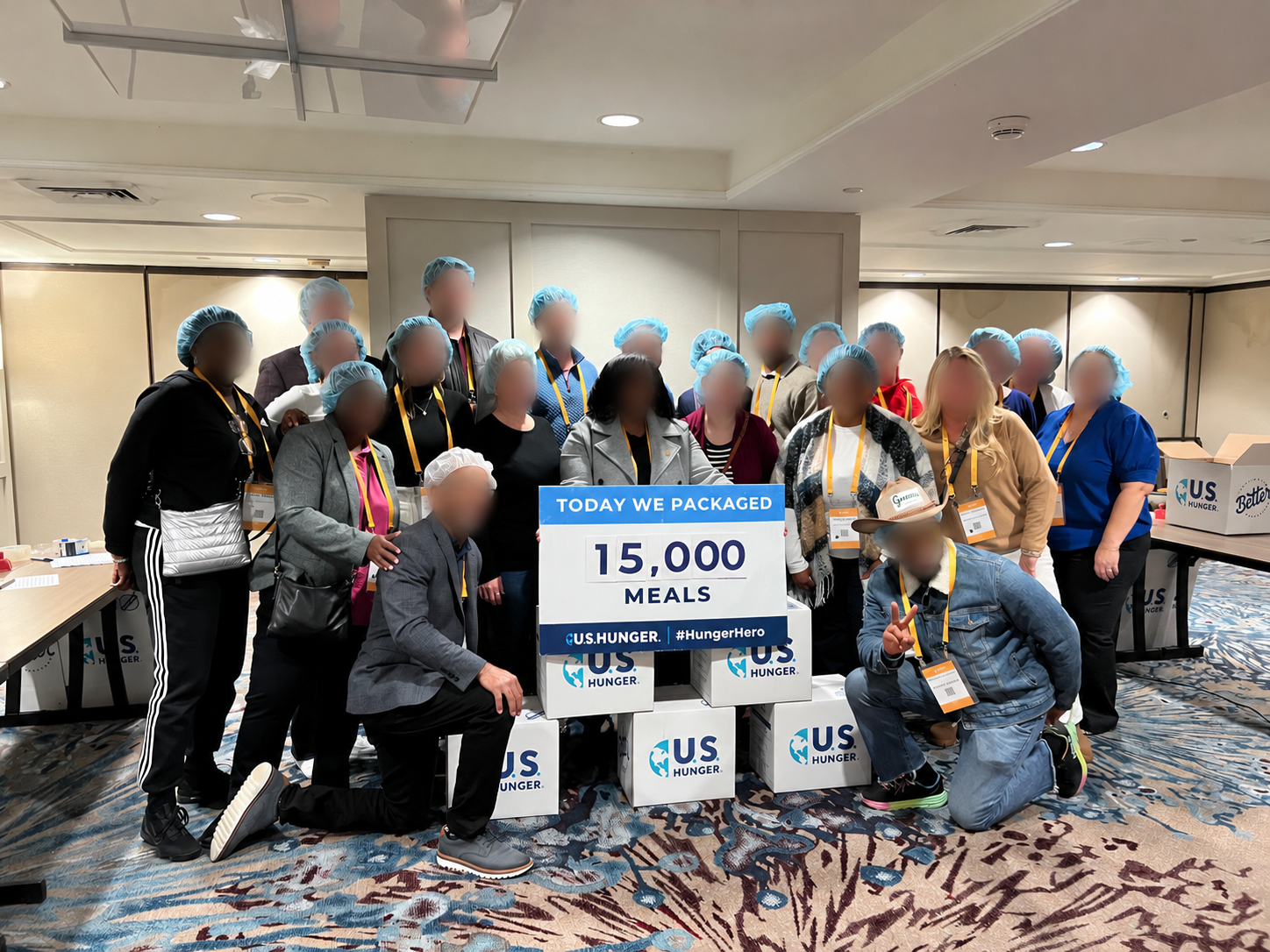 Community volunteers with a U.S. Hunger meal-packing sign; all faces obscured