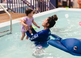 Instructor raising a smiling toddler above the water
