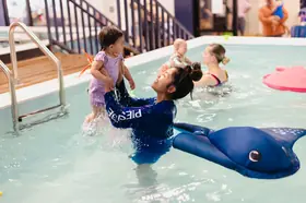 Coach joyfully lifts a toddler out of the water with splashes flying