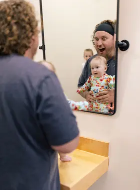 Dad playing peekaboo with his baby in the family changing area mirror