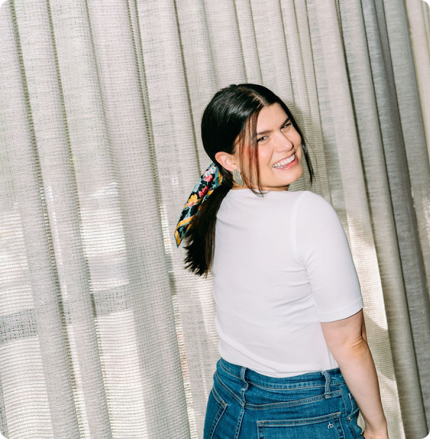 Rebecca laughing over her shoulder in front of soft curtains.