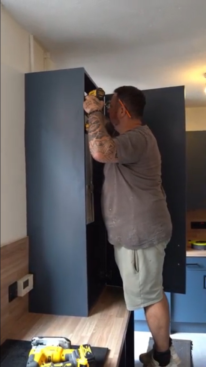 Fitter installing a kitchen cabinet