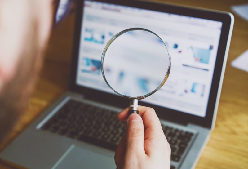 Business owner analyzing website SEO performance and Google search rankings on a laptop using a magnifying glass, representing online visibility, search engine optimization, website traffic analysis, digital marketing strategy, keyword research, and local business growth.