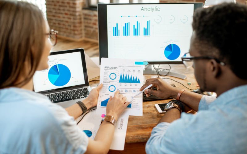 Team reviewing marketing analytics on computer screens and printed reports, analyzing data to improve lead conversion and business performance.