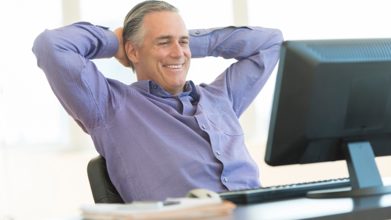 Business owner relaxing at desk with hands behind head, smiling at computer after successfully managing leads and improving conversions with an automated system.