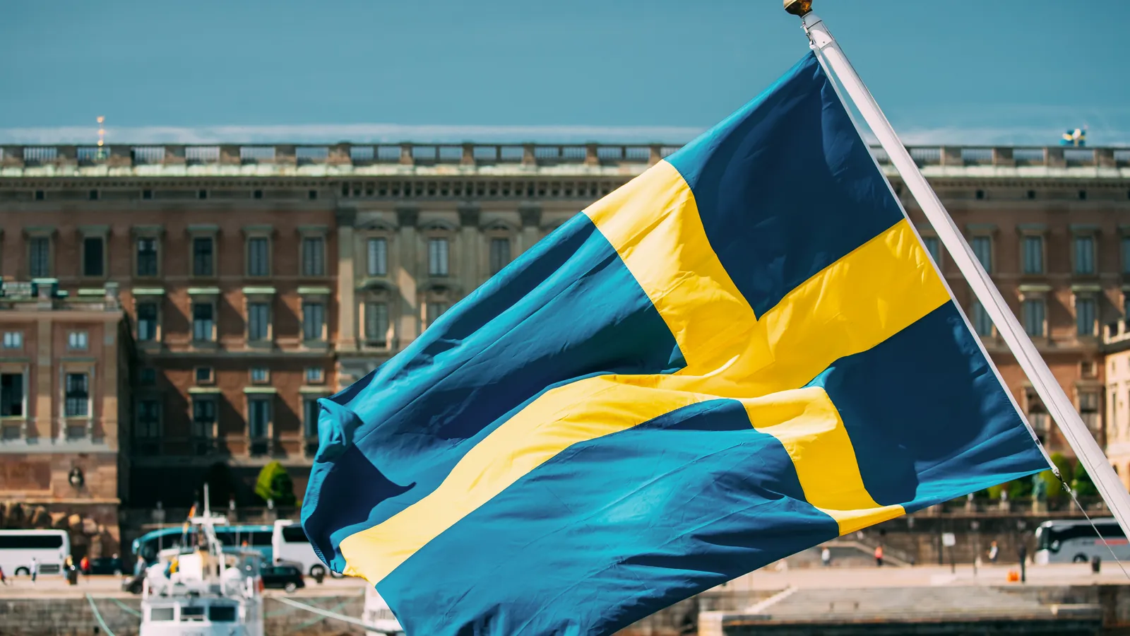 Schwedische Flagge im Wind vor einem historischen Gebäude am Wasser in Stockholm