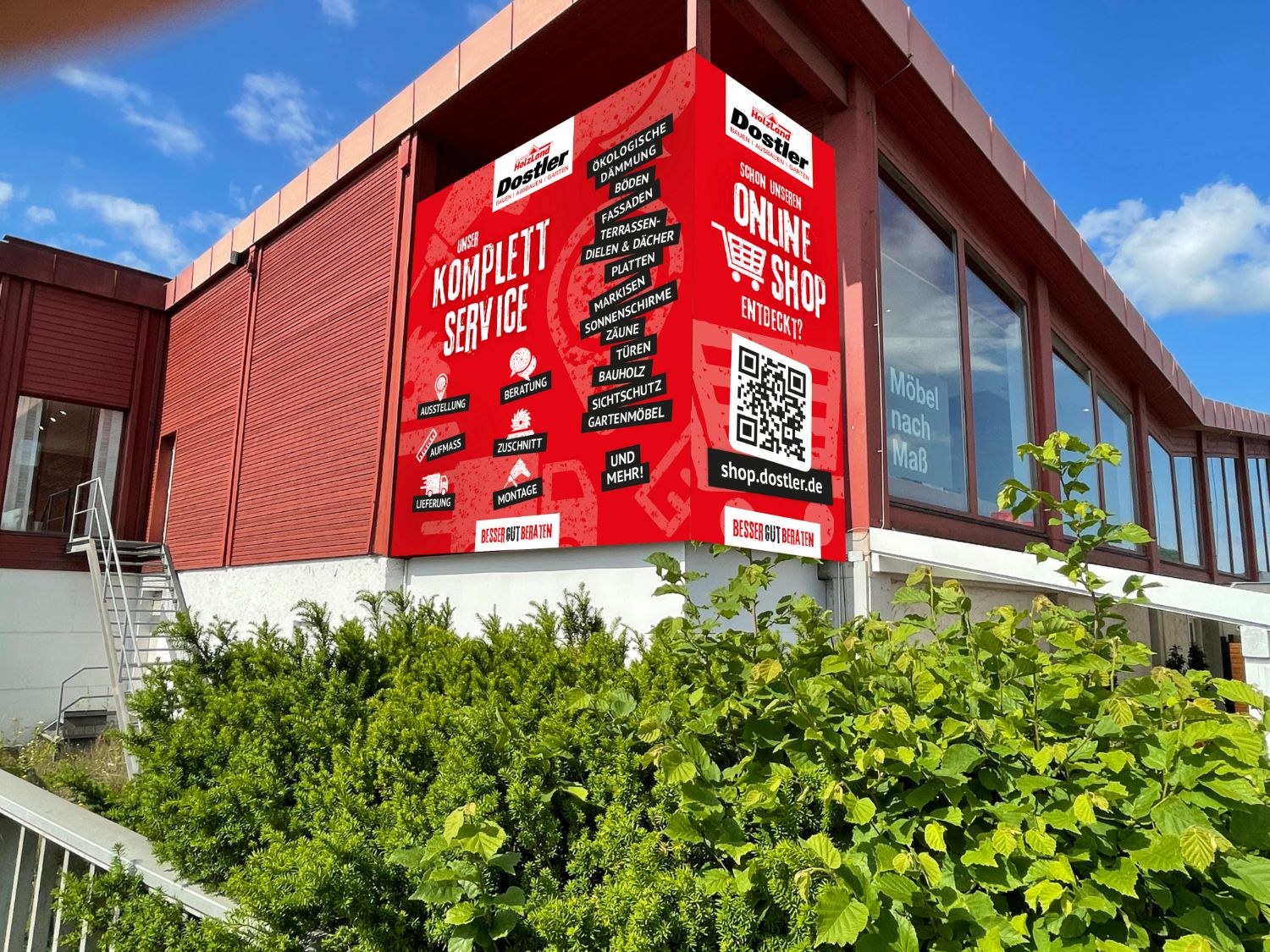 Großes rotes Banner über Eck an der Fassade von HolzLand Dostler
