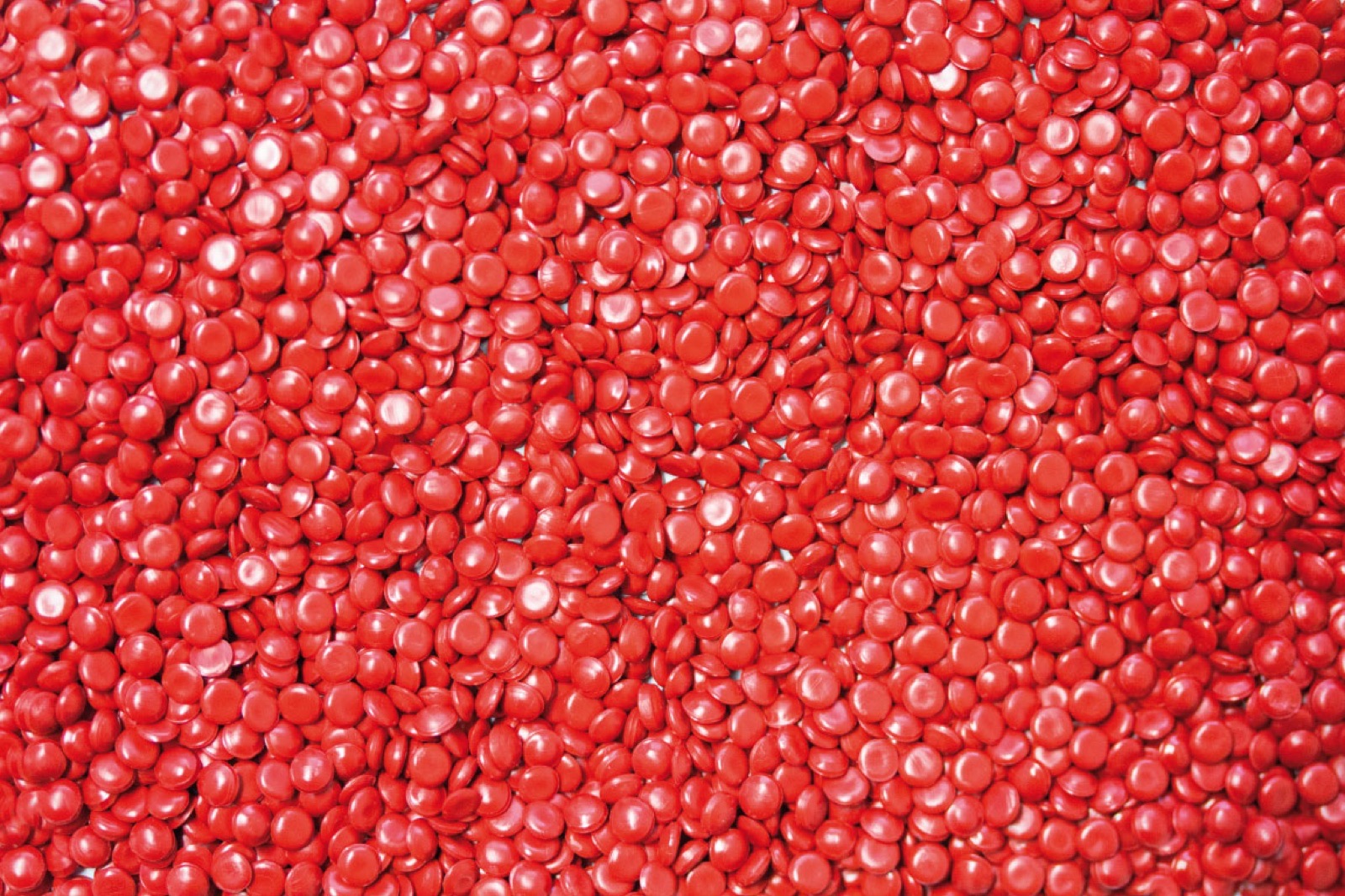 Draufsicht auf rotes Kunststoffgranulat, glänzende Linsen dicht an dicht