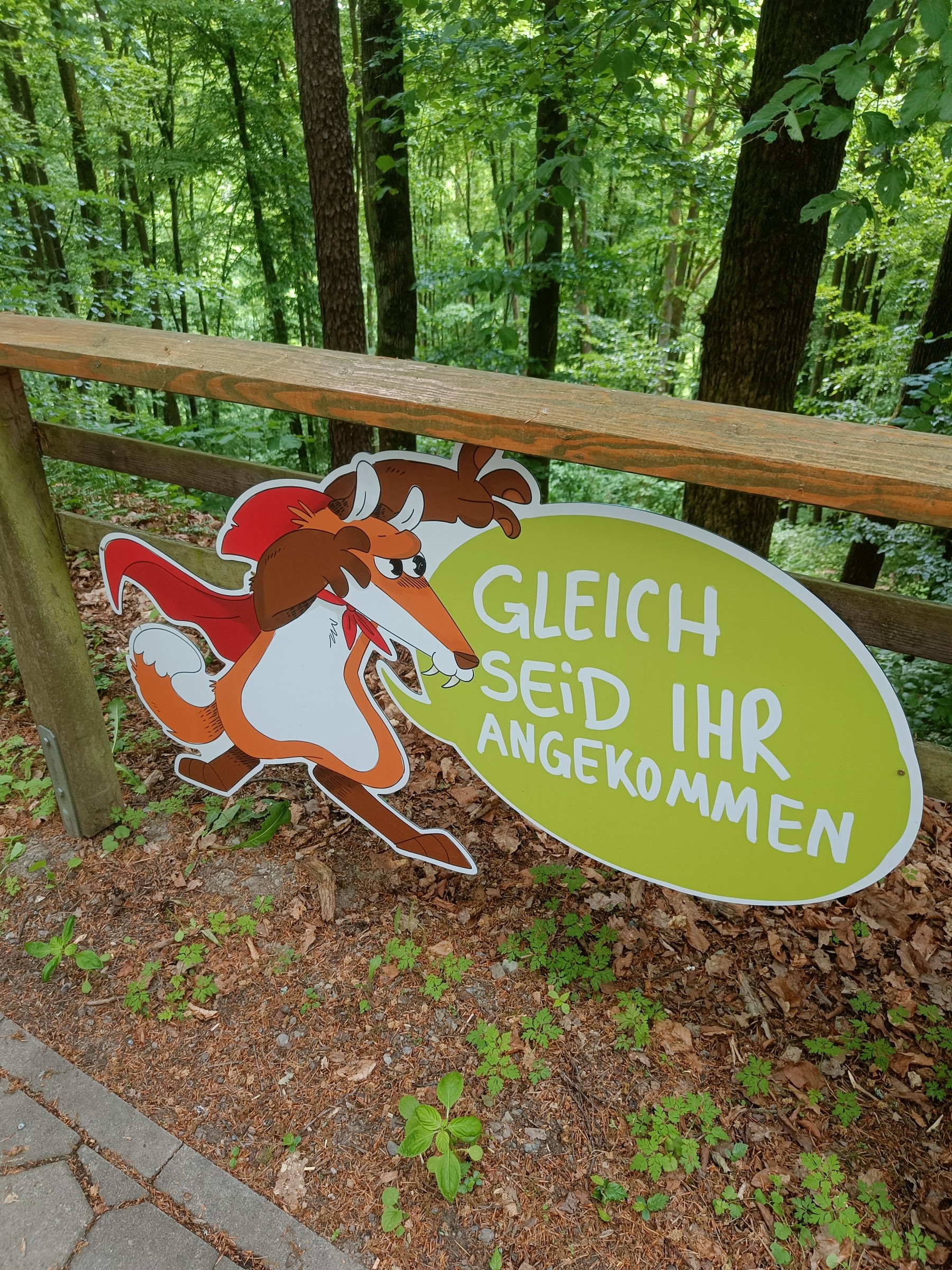 Schild in Fuchsform mit Sprechblase am Holzgeländer im Wald