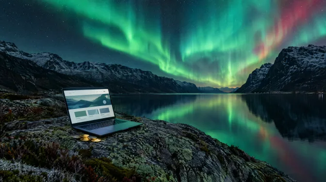 Aufgeklappter Laptop mit Website-Entwurf auf einem Granitfelsen am nächtlichen Fjord, daneben einige Münzen, darüber Polarlicht