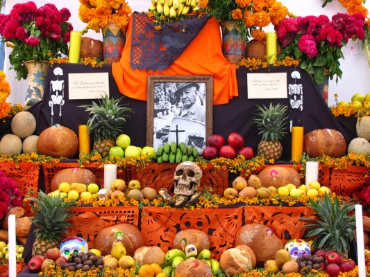 A day of the dead altar adorned with skulls, skeletons, candles, fruit, cut paper and bread.