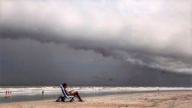 Ominous clouds form on the bay, while a beach goer is sitting reading a book.