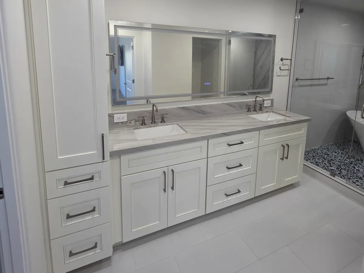 Master bath double vanity with cream cabinets, a tall linen cabinet and a veined stone top