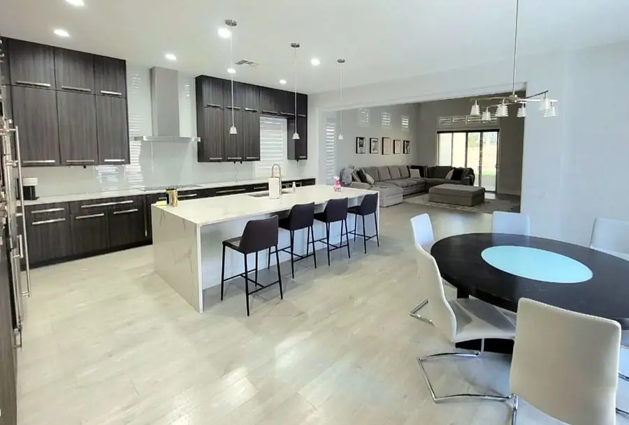 Kitchen with dark textured cabinets, a stone waterfall island and light plank flooring