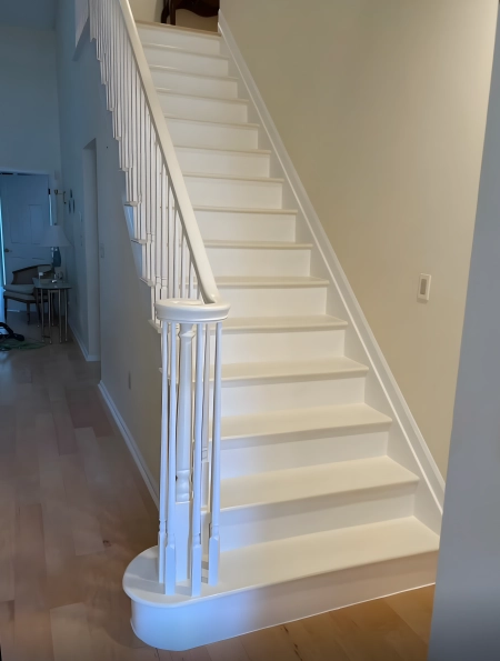 Freshly painted white staircase with wooden railings and light wood flooring in a modern home interior.