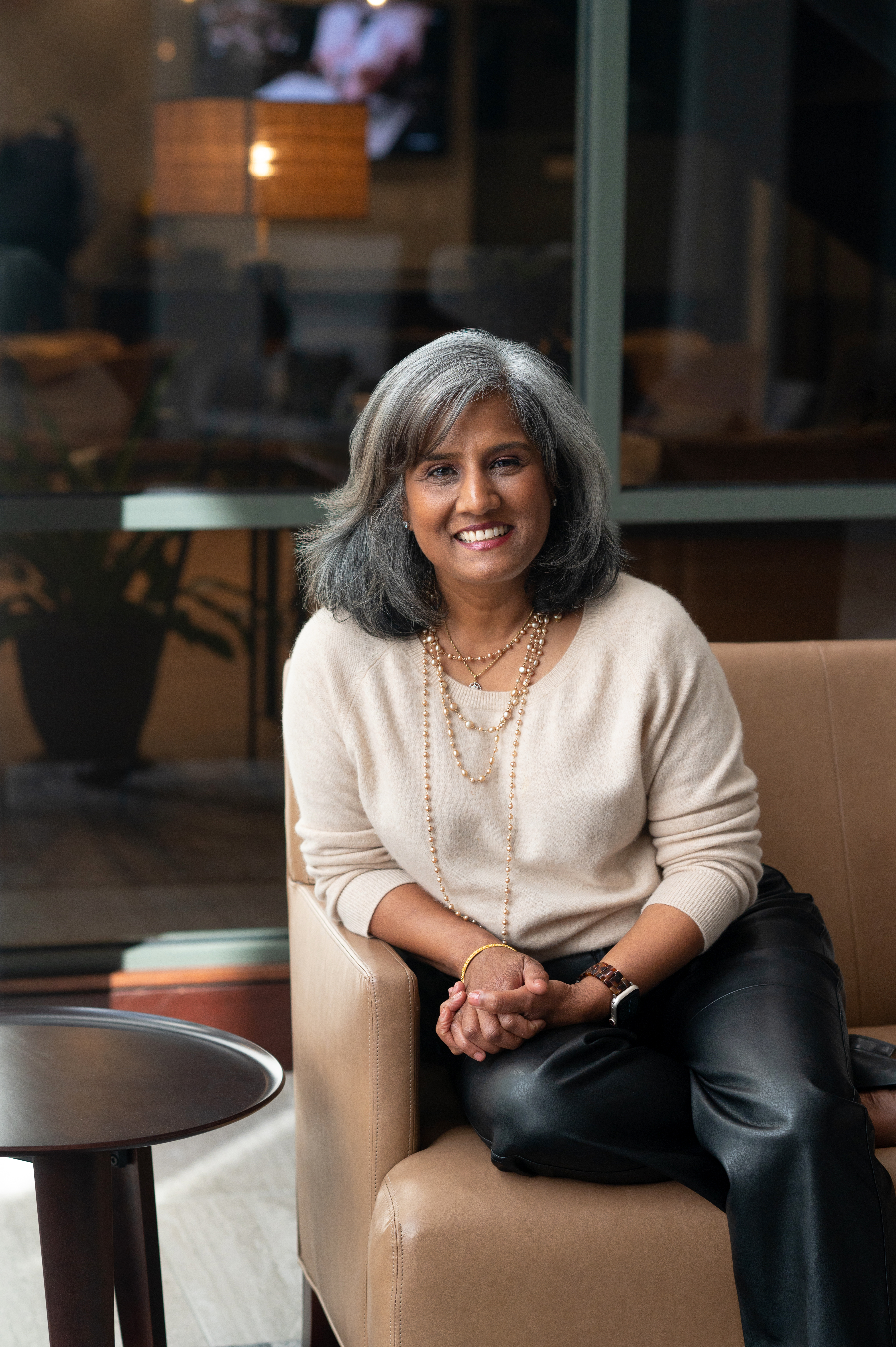 Latha Rao, fractional COO and business strategist, seated and smiling in a soft beige sweater and black leather pants
