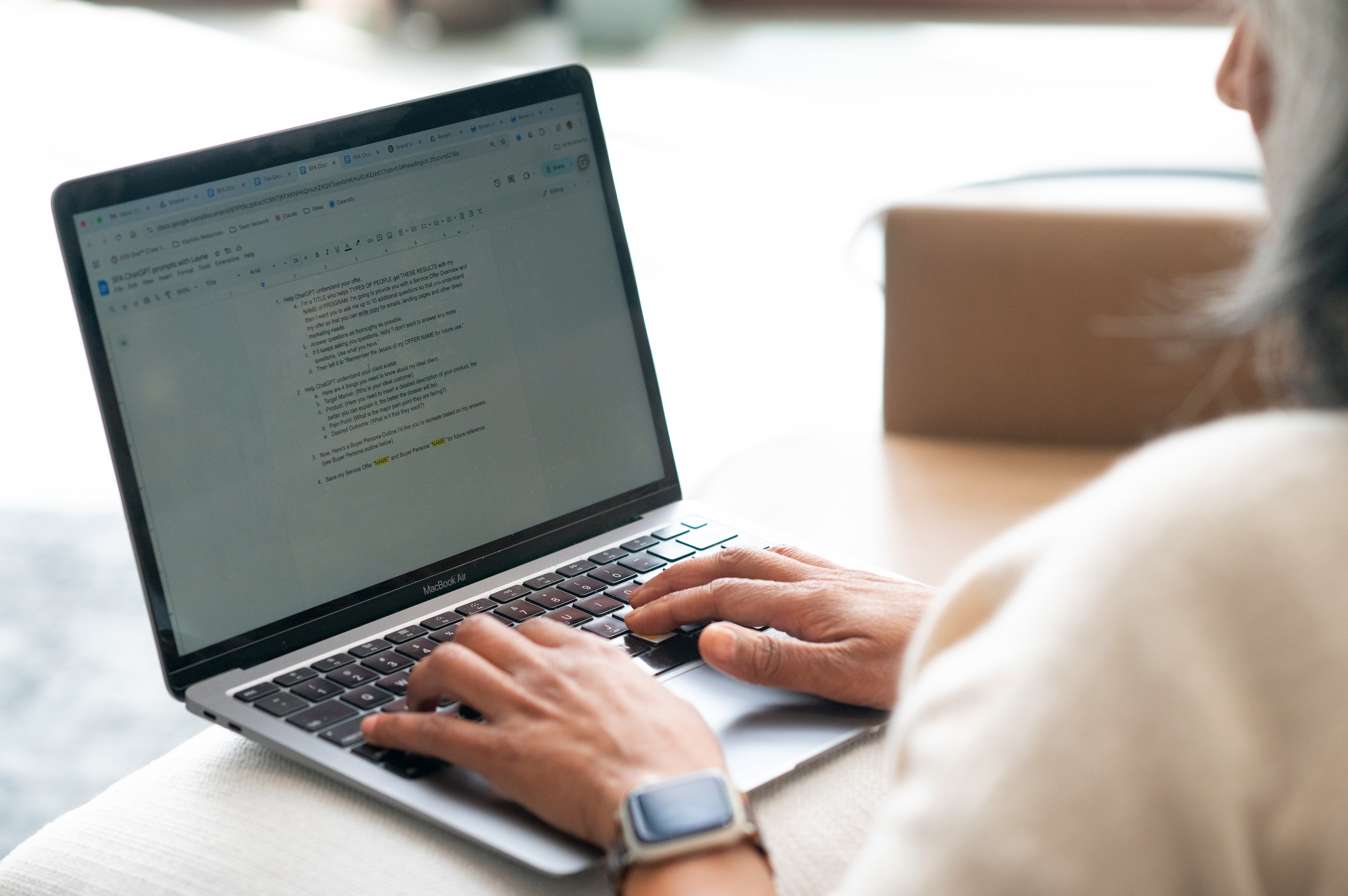 Close-up of Latha Rao working on a business strategy document on her MacBook, wearing a smartwatch and neutral sweater