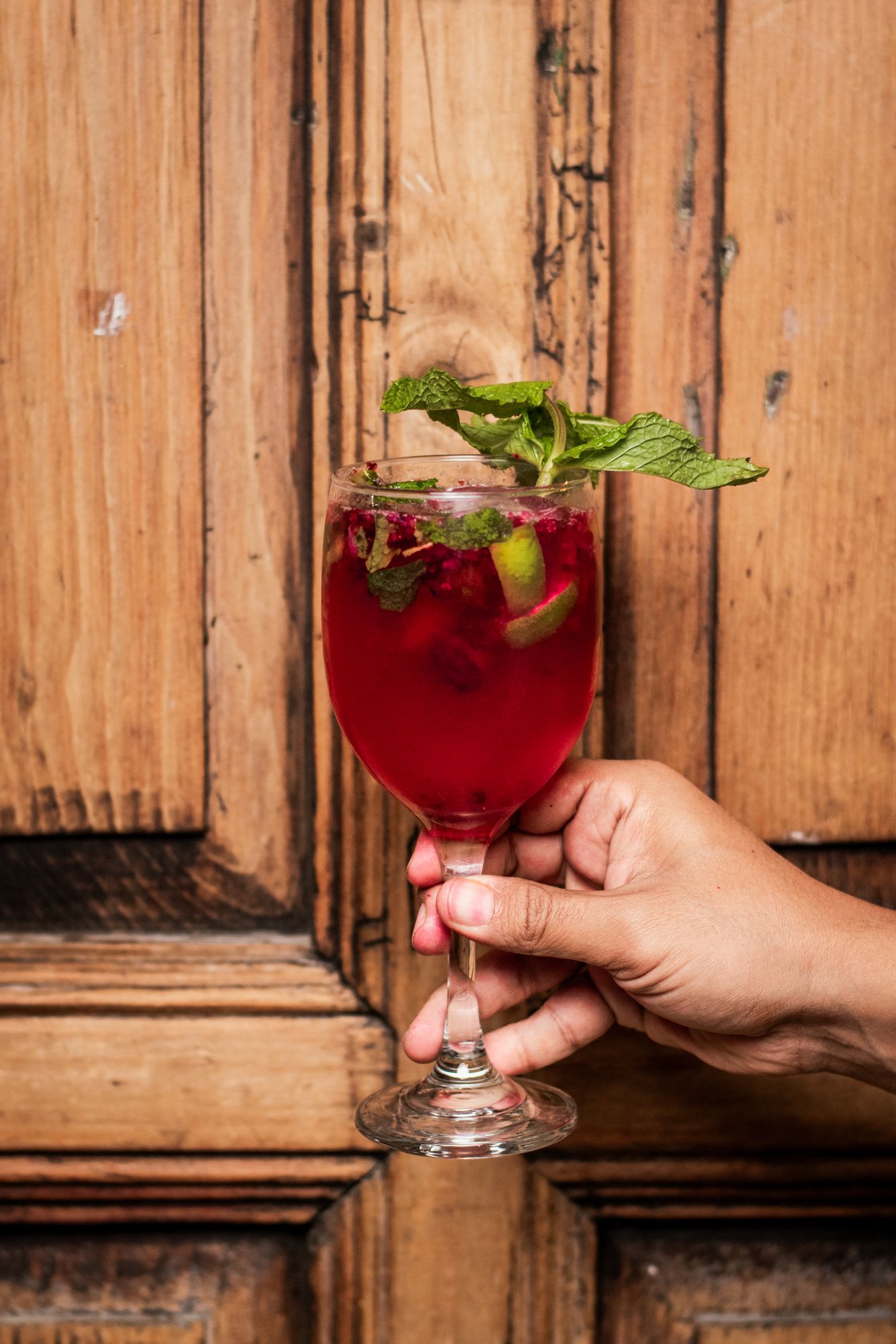 A red pox cocktail with fresh mint, held in front of an old wooden door