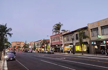 A nighttime view of a street in Pasadena, California, with cars and storefronts lining the road