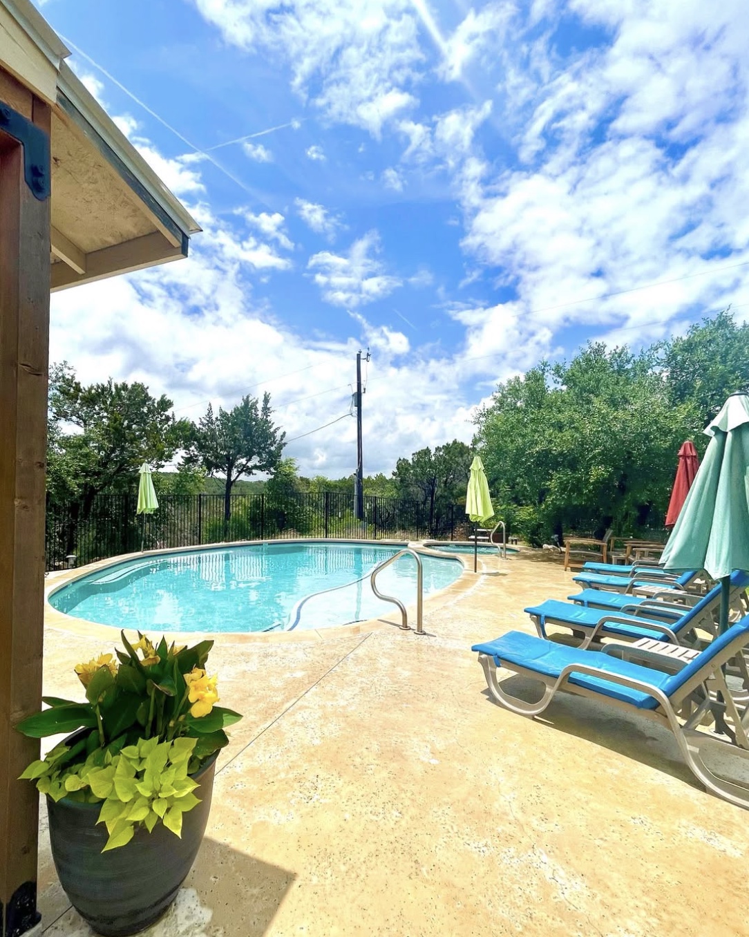 An inviting Hill Country pool with blue lounge chairs, shaded umbrellas, and open sky.