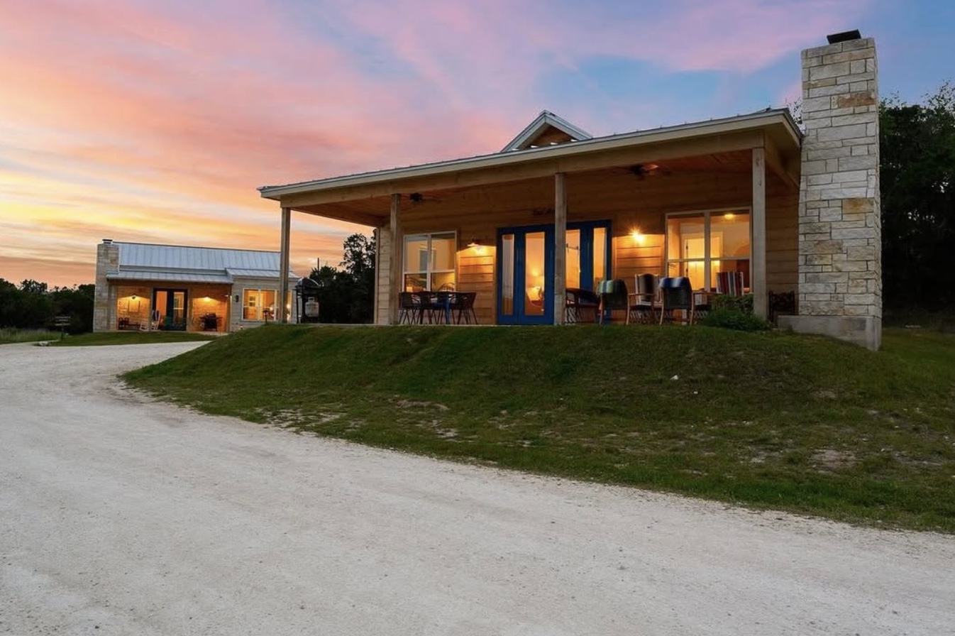 Warm lights glowing inside stone and wood Hill Country casitas beneath a pink and gold sunset.