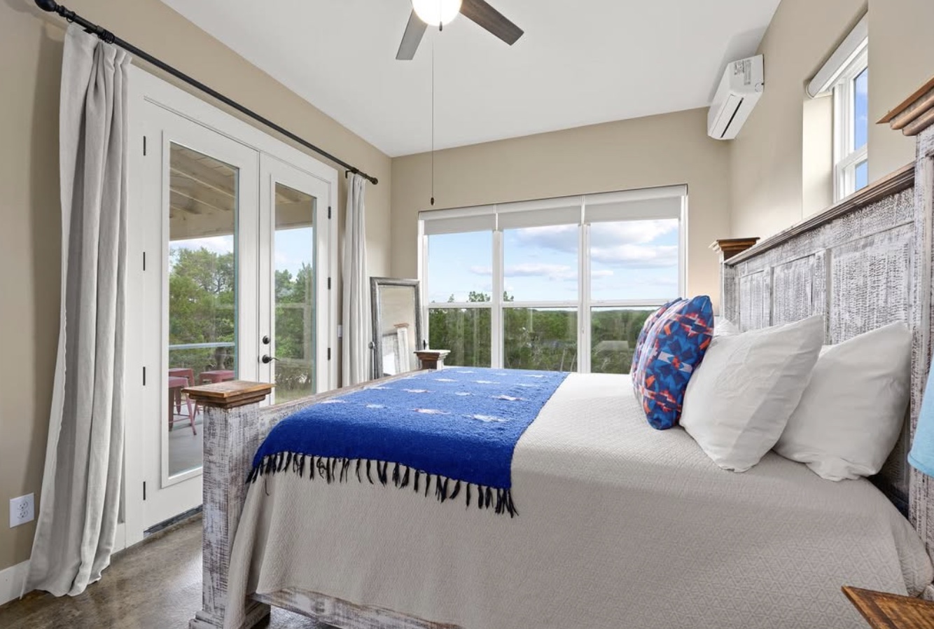 A light-filled casita bedroom with a blue throw, natural wood furnishings, and doors opening onto a porch overlooking the Hill Country.