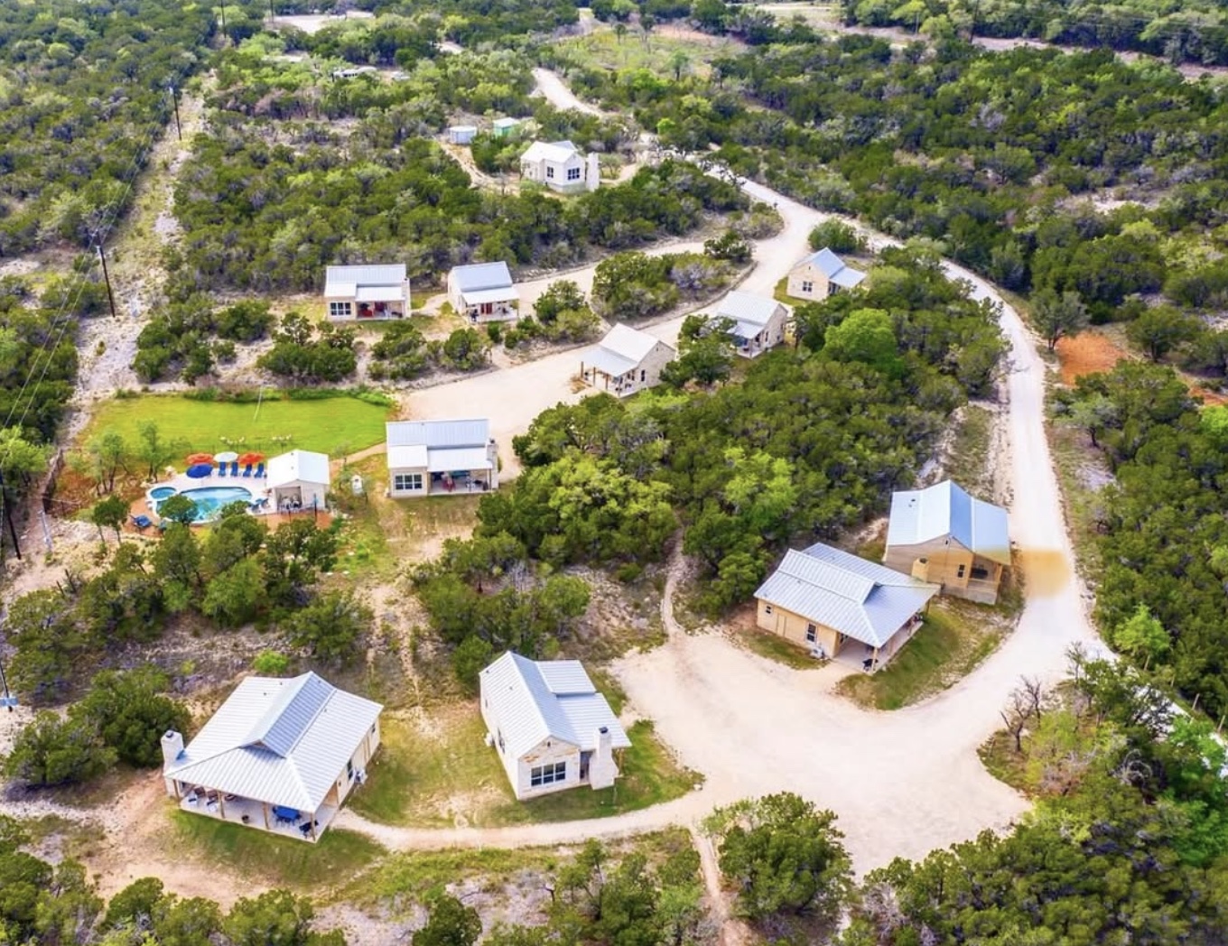 An aerial view of Hill Country Retreats, with individual casitas, winding paths, and a pool nestled among green wooded hills.
