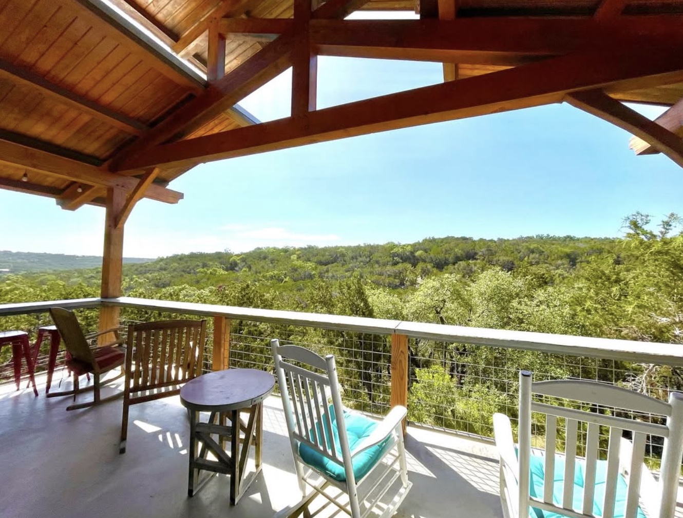 Rocking chairs on a shaded wooden porch overlooking the green Texas Hill Country.
