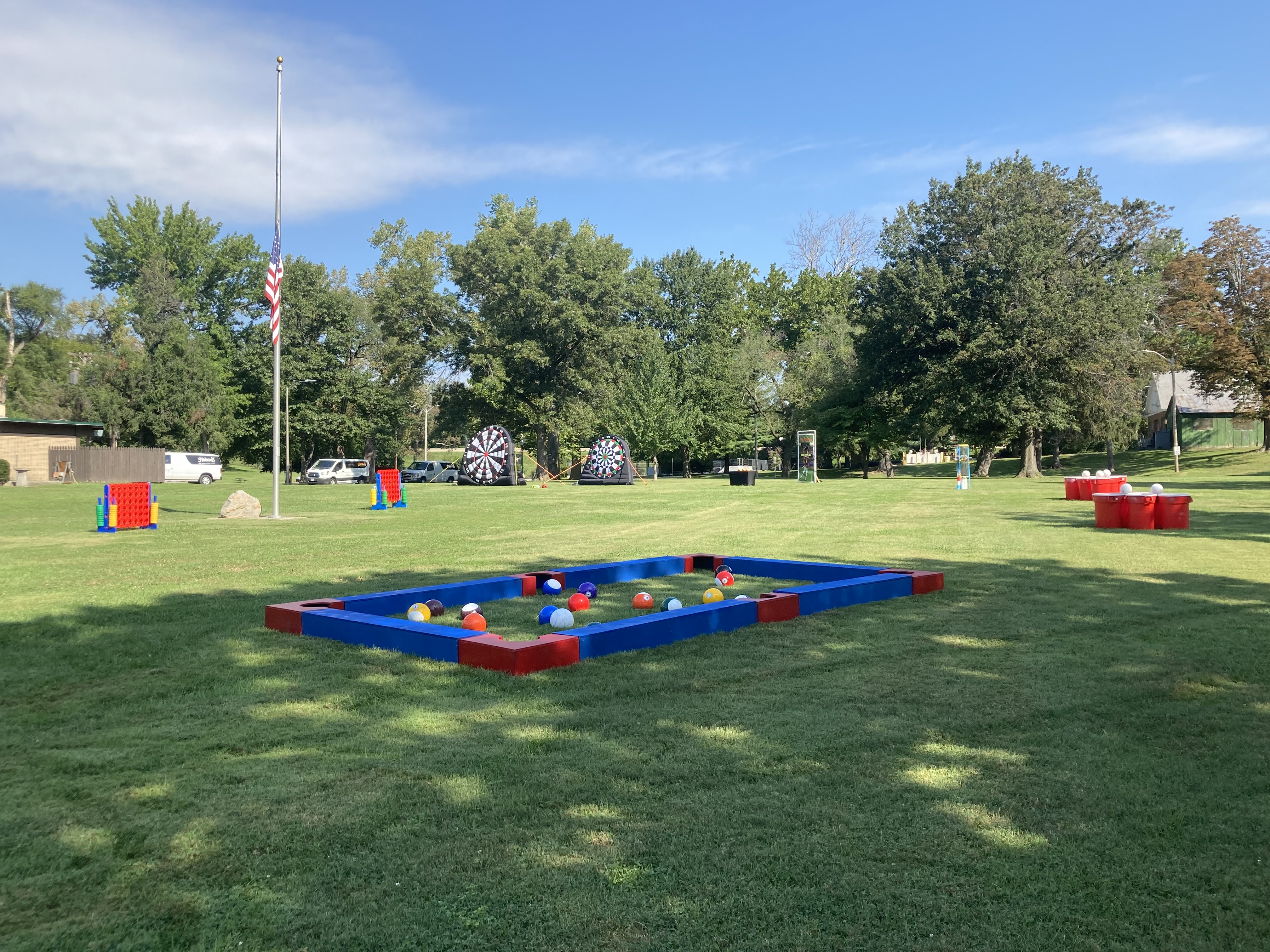 Collection of giant outdoor event games including oversized dartboards, four-in-a-row games, soccer pool, and Giant Pong for group entertainment.