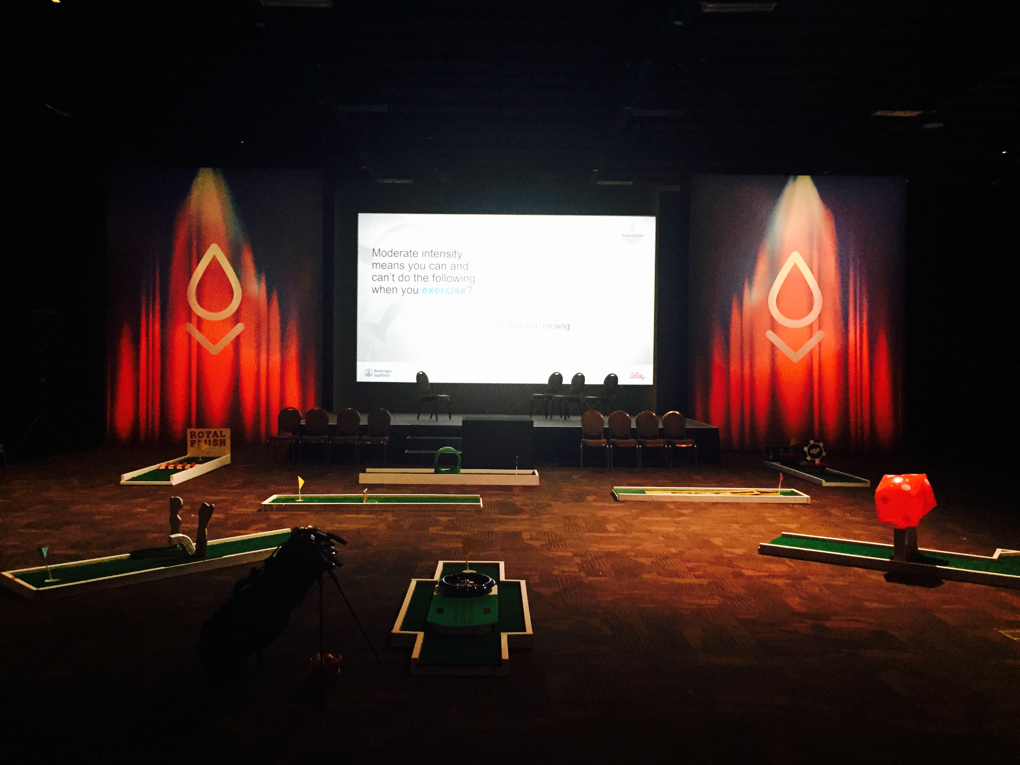 Portable miniature golf course with individual obstacles set up inside an event space.