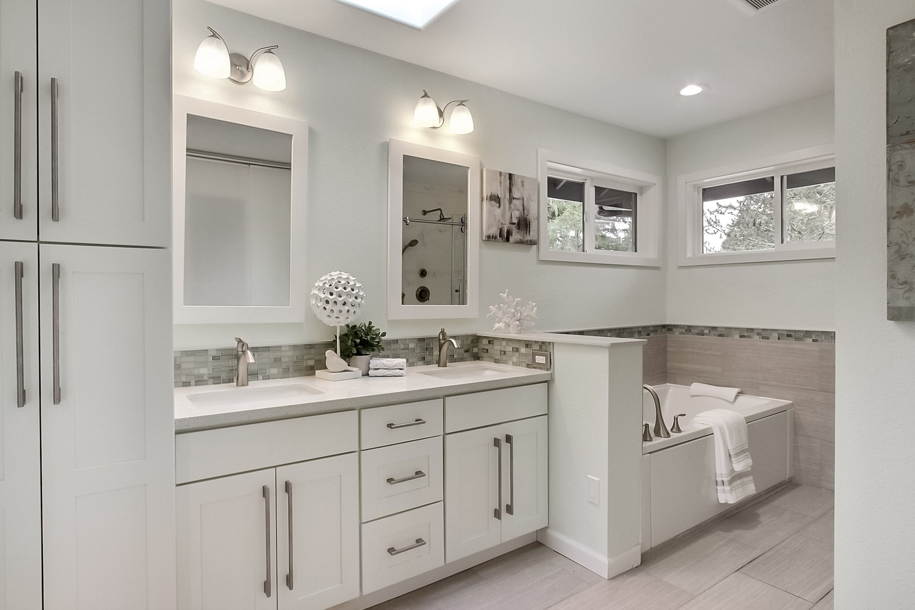 Finished master bathroom with a white double vanity, a tub, and two windows